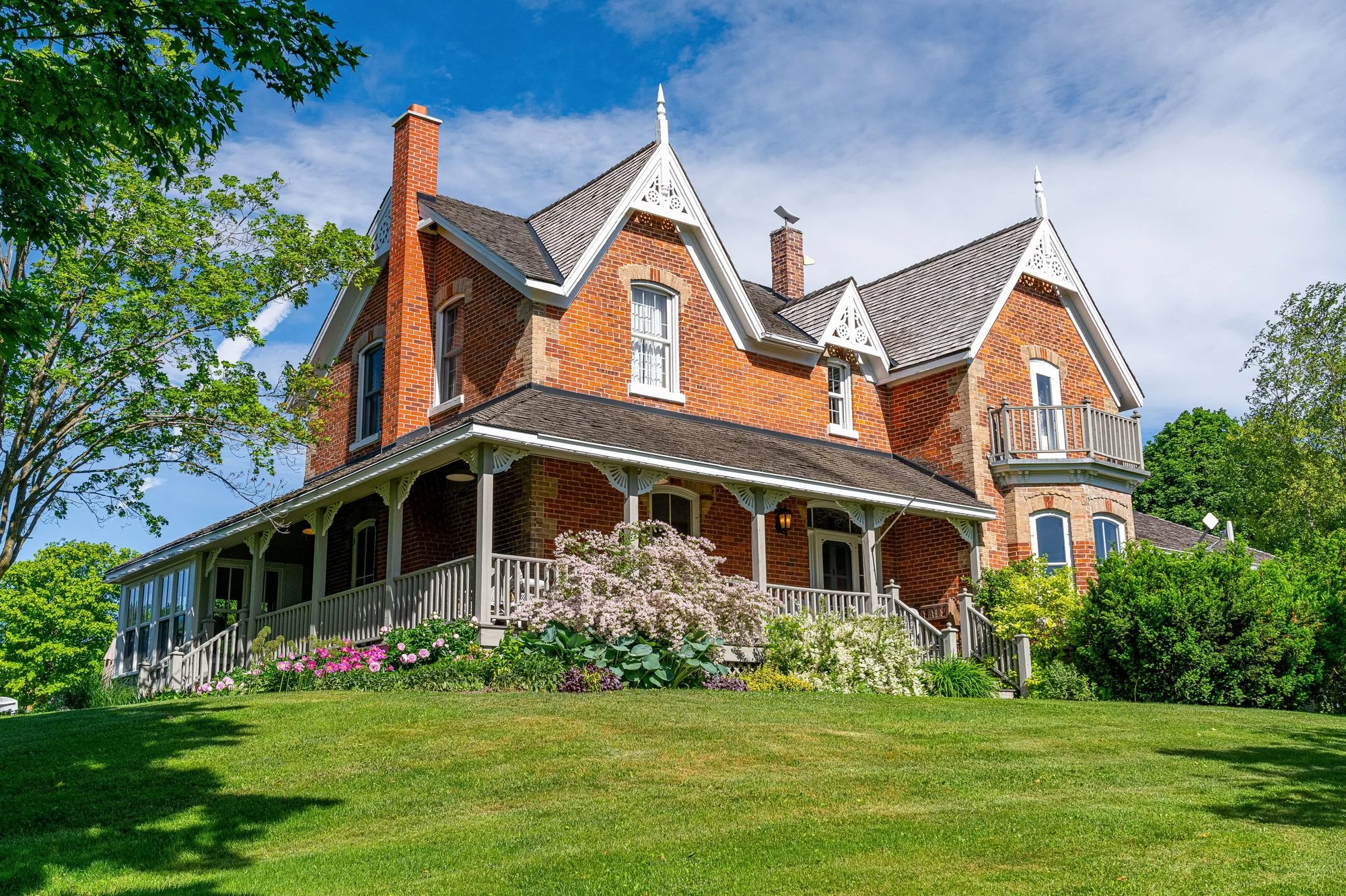 The red-brick farmhouse and wraparound porch, framed by garden greenery